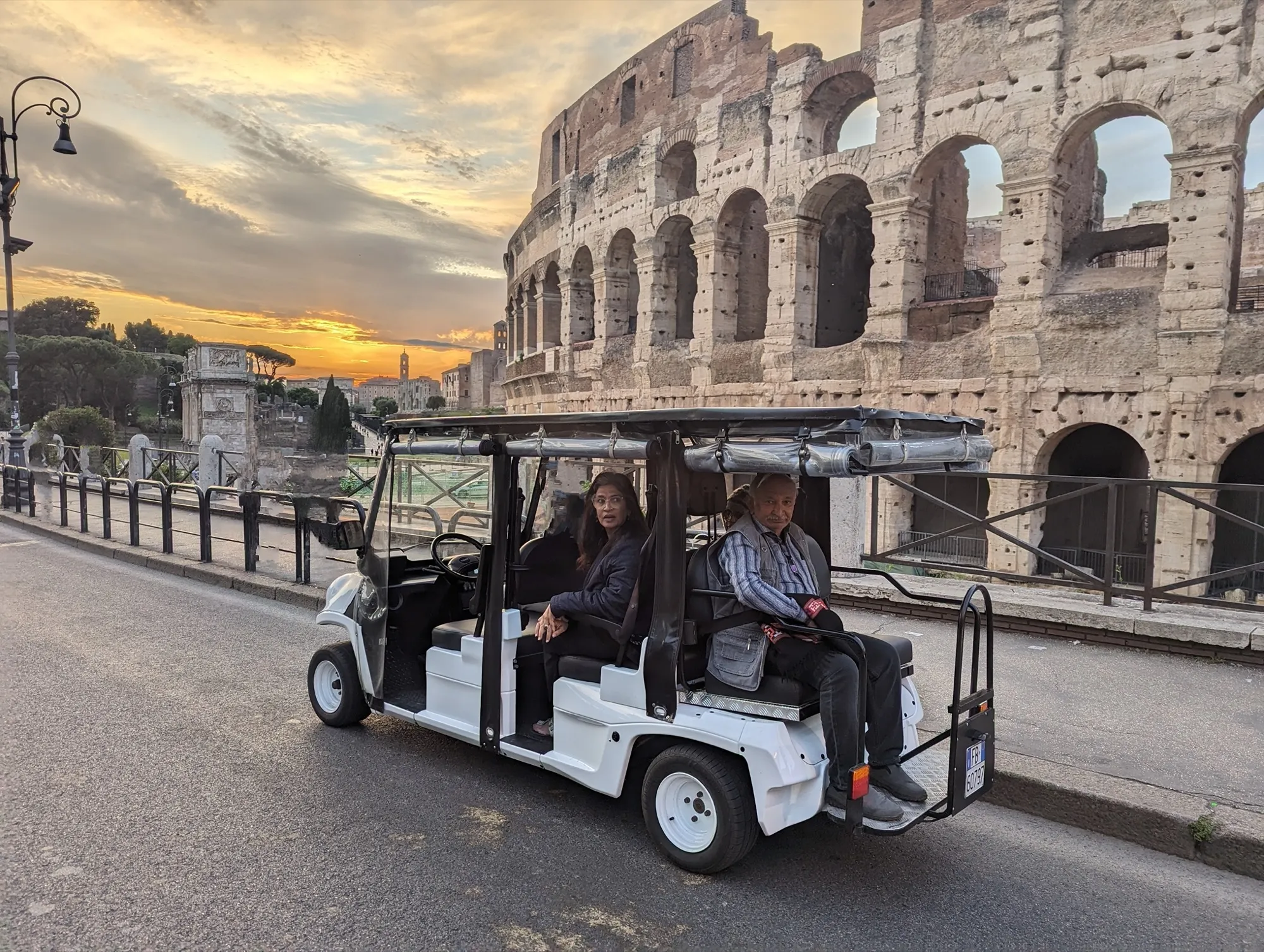 Our golf cart in front of the Colosseum at sunset, two guests on board